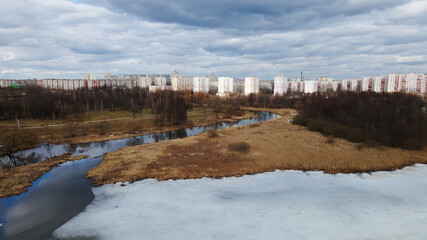Flight over the river in the spring park. Remnants of ice are visible. In the distance, people are walking along the alleys.