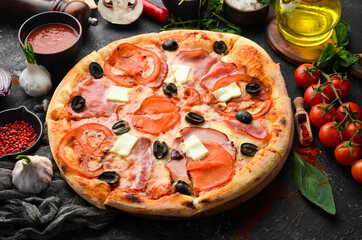Traditional pizza with bacon, tomatoes and cheese. On a black stone background. Free space for text.