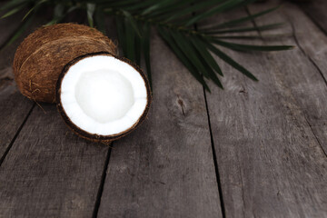 Broken coconuts on gray wooden background with palm leaf. White coconut pulp