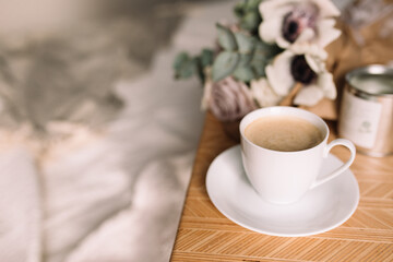 Coffee table on bed. Flowers, coffee cup and candles. Interior gray tones, plaid