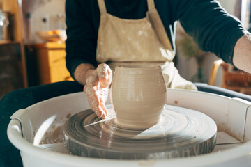 Man working on potter's wheel with raw clay with hands