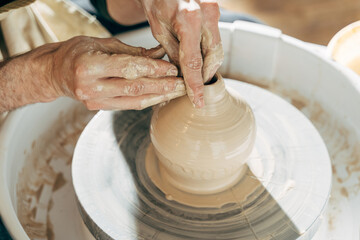 Skilled wet hands of potter shaping the clay on potter wheel