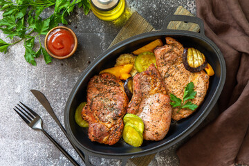 Summer Ketogenic diet lunch or dinner. Grilled pork loin on the bone with baked vegetables in a cast iron frying pan on a dark stone countertop. Top view flat lay.