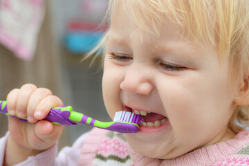 The little girl brushes her teeth in the bathroom.