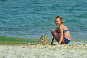 The girl builds a tower of sand on the seashore.