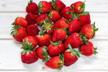 A pile of beautifully colored and freshly picked strawberries from the garden, photographed from above on a wooden background. The concept of healthy, vegetarian and dietary food