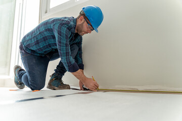 Builder man measuring for the installation of the wooden floor in the renovation of a house