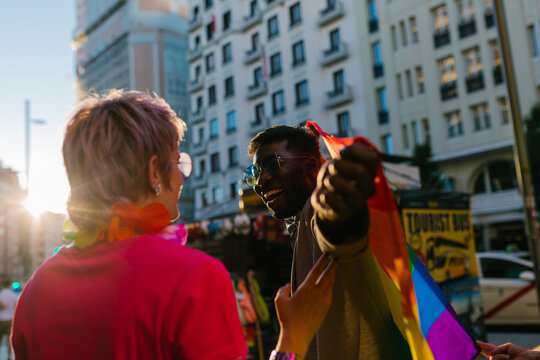 Happy multiracial couple raising LGBT pride flag in street in daylight