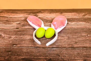 Bunny ears and Easter eggs lie on a brown wooden texture.
