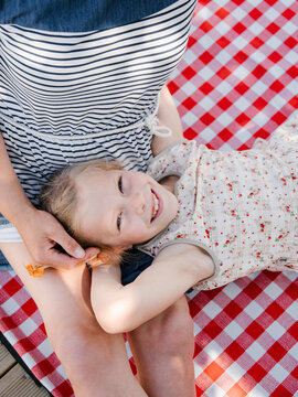 Happy daughter resting on mothers laps on plaid near wheelchair