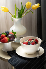 Breakfast table with tulips, bowl with porridge and berries.