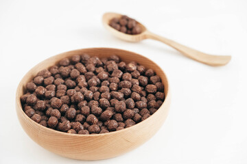 Chocolate corn balls in a wooden bowl and spoon on a white background. Copy, empty space for text