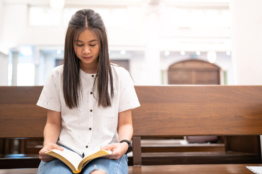 Asian woman is reading the Holy Bible and praying in a Christian church.