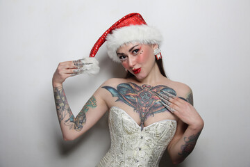 Portrait of beautiful tattooed young woman in Santa hat and corset, with fancy makeup and nails