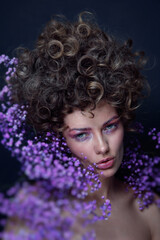 Vintage style portrait of beautiful young woman with fancy hairdo and violet flowers around her face, soft focus, grainy