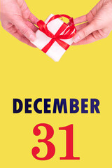 December 31st. Festive Vertical Calendar With Hands Holding White Gift Box With Red Ribbon And Calendar Date 31 December On Illuminating Yellow Background. Winter month, day of the year concept.