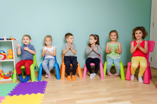 Kids are sitting on the colorful chairs, clapping hand - Powered by Adobe