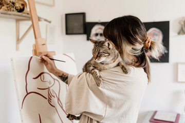 Young female artist painting on her studio holding cute cat