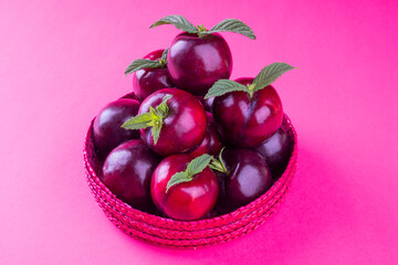 Healthy fruit and pink color concept: A group of purple red tropical plums with green leaves in a pinkish basket. Natural food background in fuchsia color with copy space