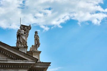 A view of sculptures on top of the Tuscan Colonnades and blue cloudy sky at St. Peter's Square in the Vatican city in Rome, Italy.