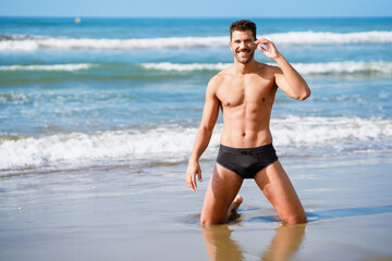 Fototapeta na wymiar Handsome man on his knees smiling on the sand of the beach