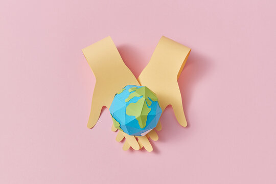 Papercraft two crossing hands are holding planet.