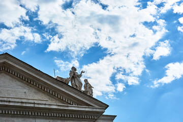 Obraz premium A view of sculptures on top of the Tuscan Colonnades and blue cloudy sky at St. Peter's Square in the Vatican city in Rome, Italy.