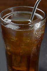 Tall glass of iced coffee. Close-up view of the top of the glass. Focus on the front wall of the glass. Black background. Water drops on a glass.
