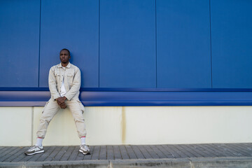 Fototapeta na wymiar Chico negro apuesto posando delante de una pared azul y puerta blanca