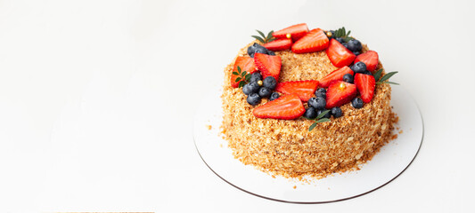 Honeycake with a lot of crunchy crumbs and decorated with strawberries and blueberries. White background