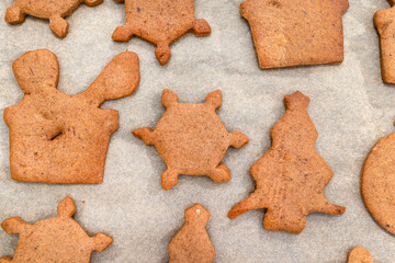 Baked gingerbread cookies in various shapes without decorations, lying on baking paper, top view.