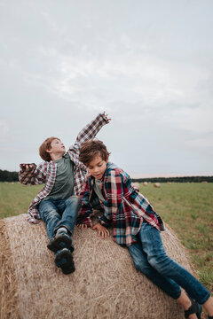 Two brother sitting on a haystack in the field.