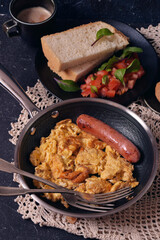 Homemade hot omelet in a frying pan. Homemade bread and tomatoes on a black plate