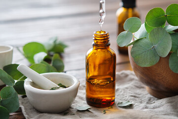 Bottle of eucalyptus oil, mortar and wooden bowl of green eucalyptus leaves. Close up of a drop of...