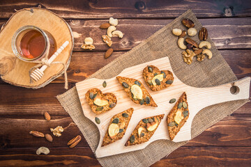 Homemade apple granola bars, decorated with dried apple and pumpkin seeds, lying on a wooden slat on wooden background, top view