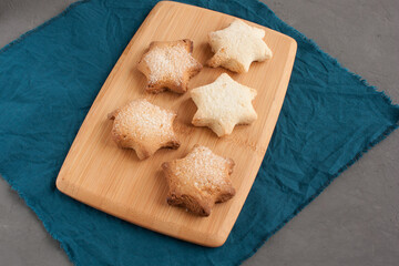 Delicious homemade cookies in the shape of stars sprinkled with sugar. Laid out on a kitchen board on a dark gray background.