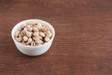 Fried salted pistachios in a white bowl on a wooden table