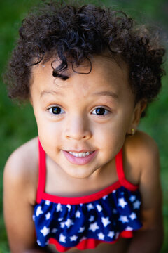 Closeup portrait of a mixed race toddler girl with curly hair wearing a red white and blue bathing suit