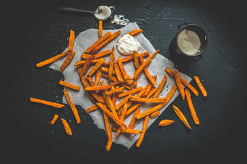 Sweet potato fries with sour cream dip on black background, top view
