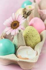 Obraz na płótnie Canvas Box with pastel-colored easter eggs, candles in eggshell and spring flower blossoms as Easter decoration, vertical