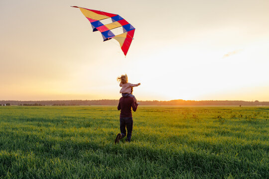Father and kid having fun with kite in field