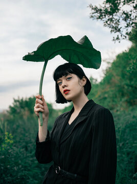 Portrait of a young woman with big leaf outdoors