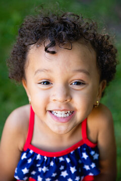 Closeup portrait of a mixed race toddler girl with curly hair wearing a red white and blue bathing suit