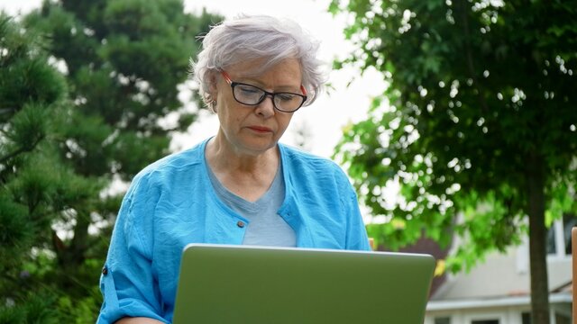 Beautiful elderly woman in her garden working at home on a laptop