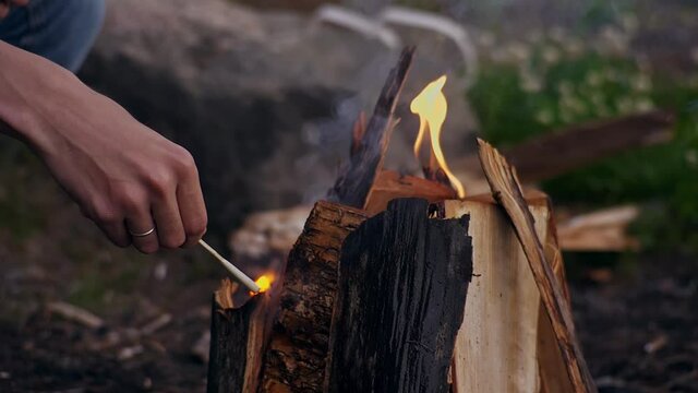 Young traveler lights a bonfire with a long match in nature in the forest. Hands with a wedding ring close up. Camping. Tourism. Travel