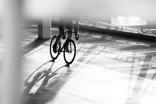 Cyclist Urban Bike Racer in car park environment, monochrome contrast light and shadows on ground silhouette