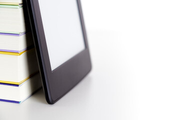 Corner of a stack of books and an electronic reader with a blank screen