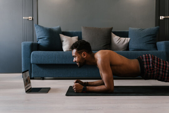 Ethnic man doing plank during online workout