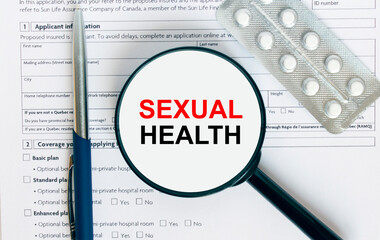 Magnifying glass with text Sexual Health inside lies on medical documents with pills and a blue metal pen