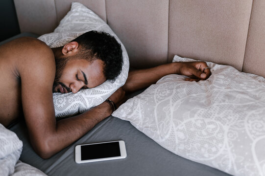 Ethnic Guy Sleeping On Bed Near Smartphone